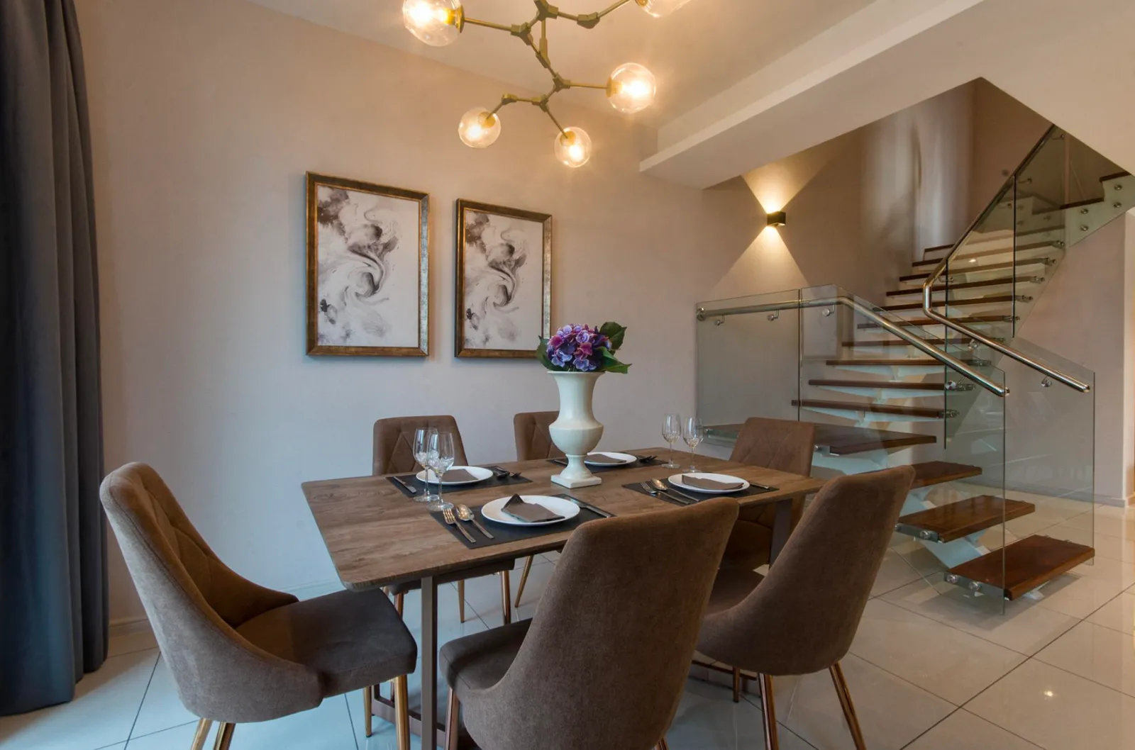 Ruang makan unit duplex Elysia Park Residence dengan tangga berpagar kaca menuju tingkat atas
