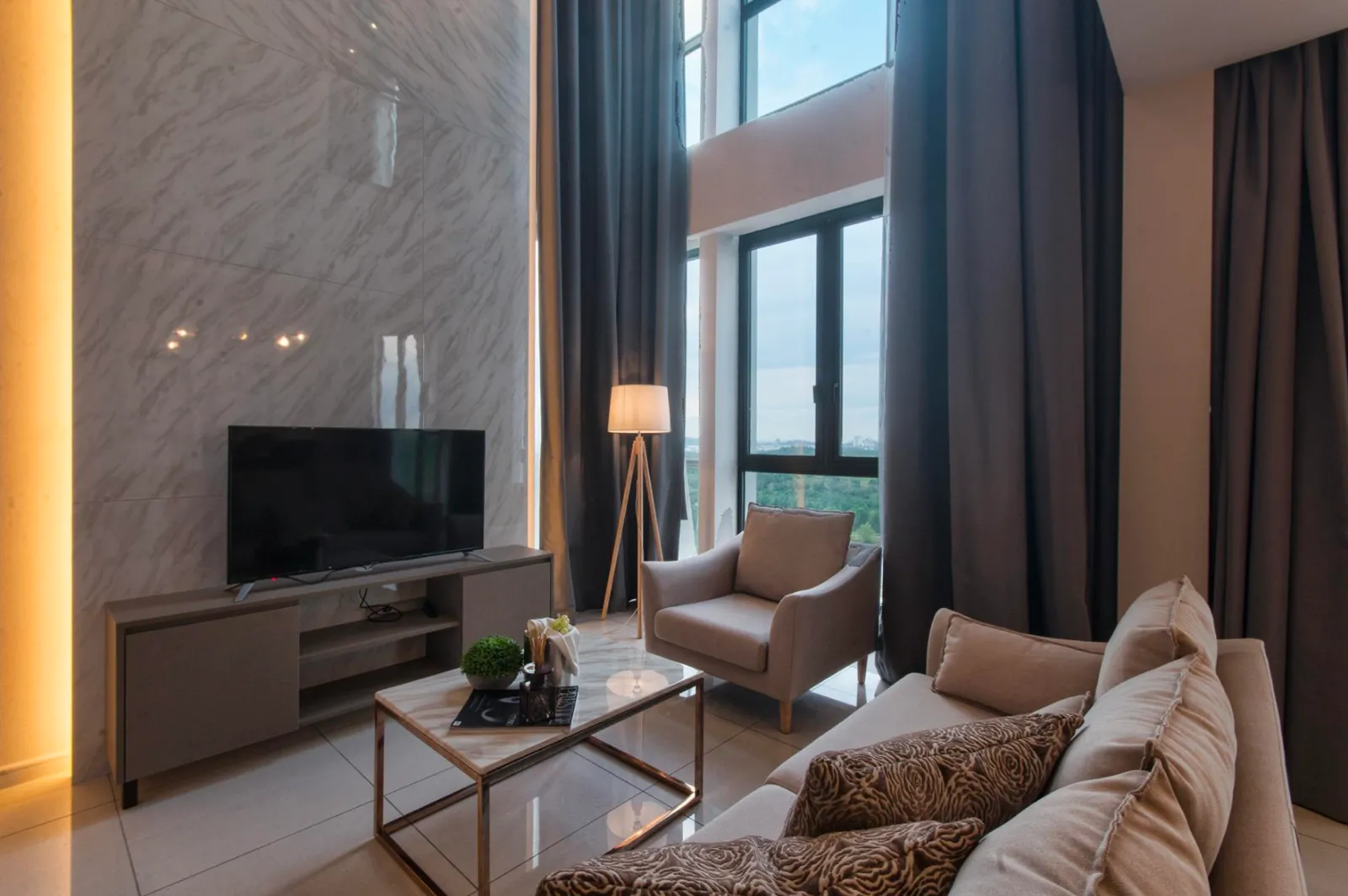 Ruang tamu bersiling tinggi di unit duplex Elysia Park Residence dengan dinding fitur marmar dan lampu lantai