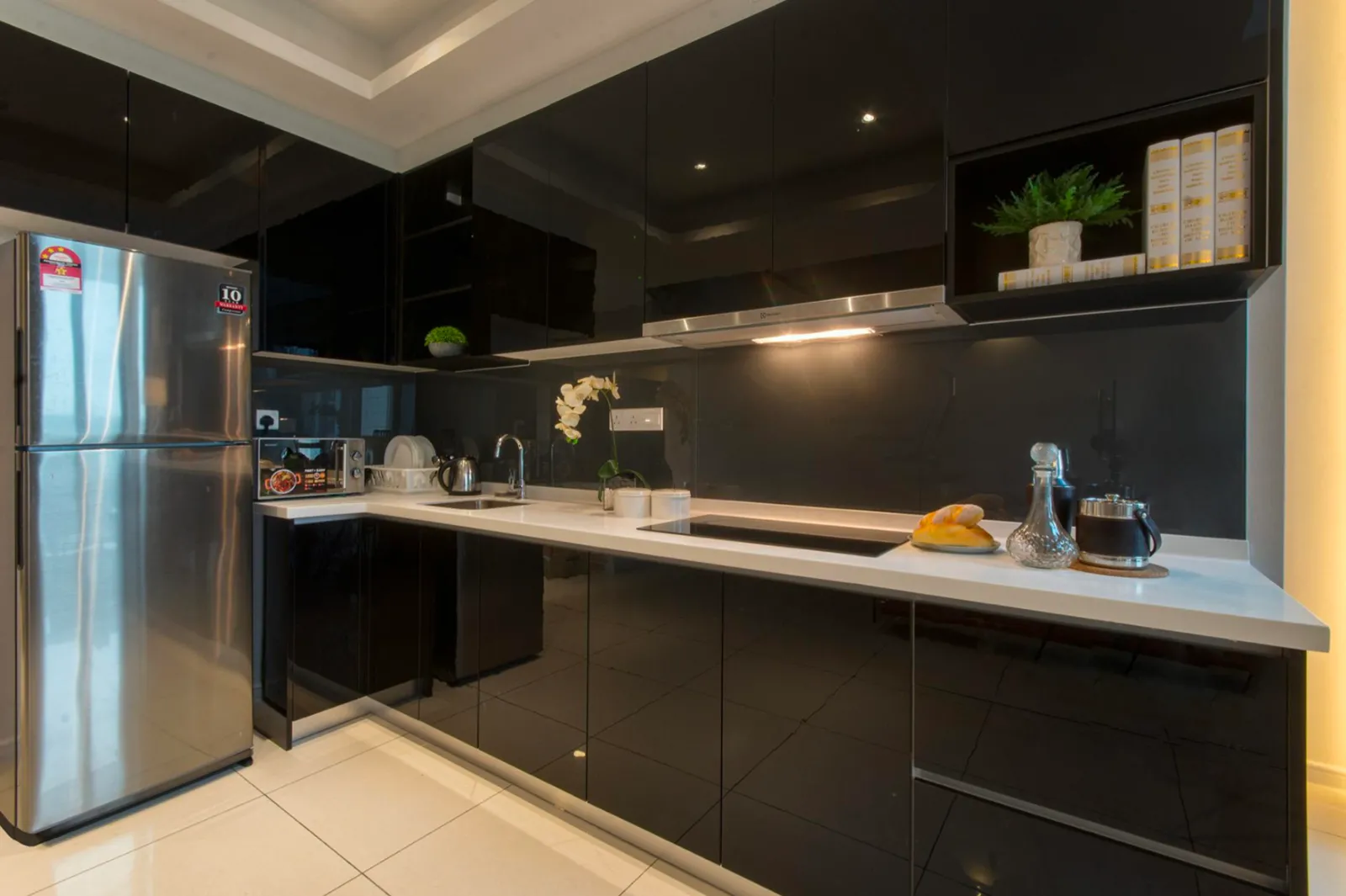 Hiasan dalaman dapur gloss hitam moden di Elysia Park Residence dengan peti sejuk keluli tahan karat dan peralatan atas kaunter