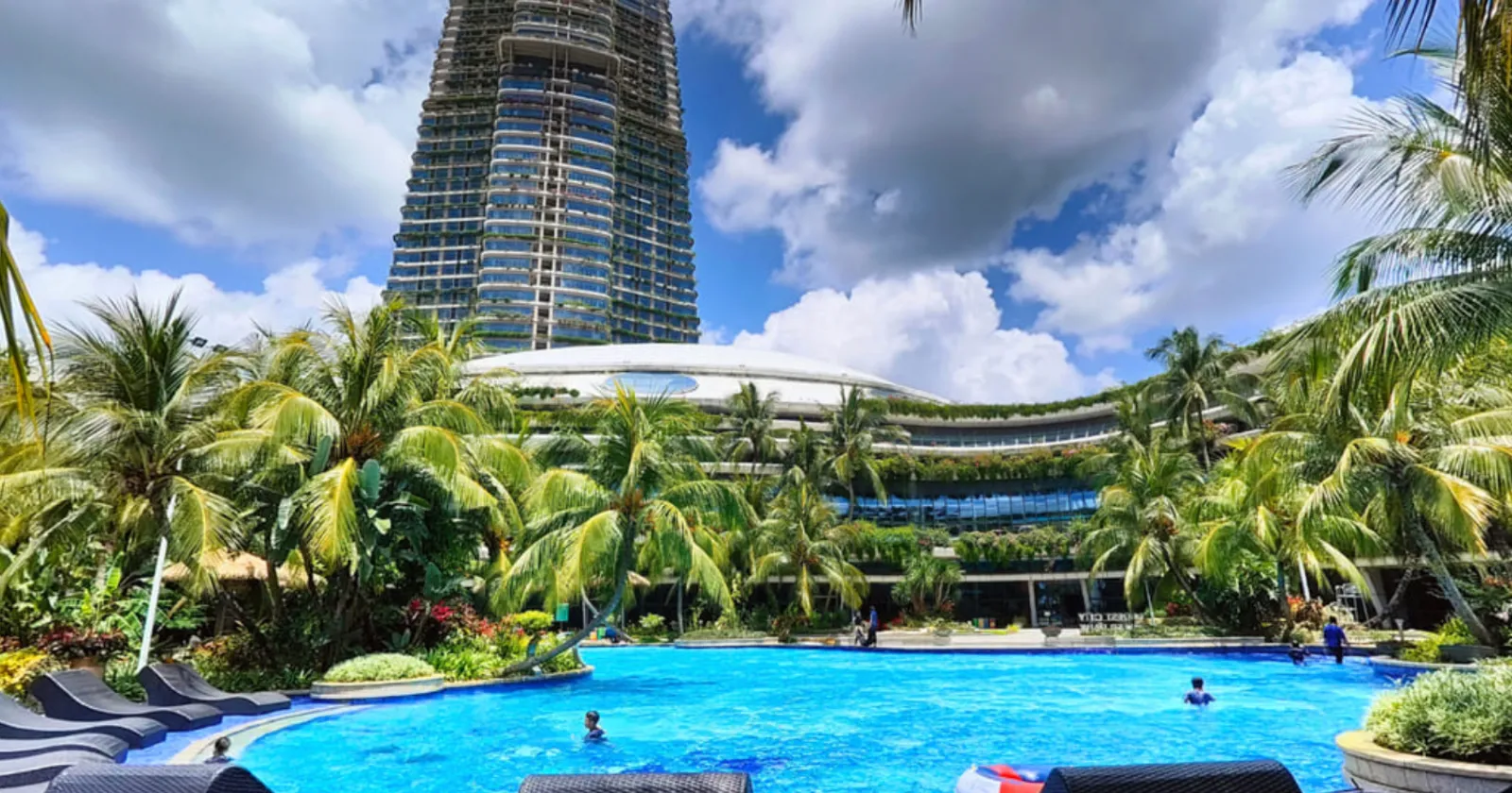 Kolam renang resort Phoenix Golf Hotel dikelilingi pokok kelapa dengan menara Nigella Park sebagai latar belakang